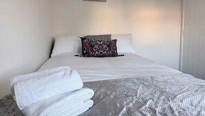 A neatly made bed with white linens, a patterned pillow, and a folded white towel on the bed. - 3-Bed House, Sleeps 7 with Parking & Garden (Wishaw)
