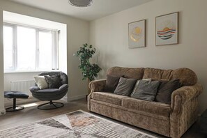 Een woonkamer met een bank, fauteuil en een groot raam.