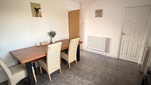 A dining area with a wooden table and four chairs, a radiator, and a white door. - Hidden Cozy 2-Bedroom Haven (Stoke-on-Trent)