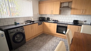 A compact kitchen with wooden cabinets, a washing machine, a microwave, and a dining area with a table and chairs. - Hidden Cozy 2-Bedroom Haven (Stoke-on-Trent)