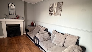 A living room with a long sofa, fireplace, and wall art. - Hidden Cozy 2-Bedroom Haven (Stoke-on-Trent)