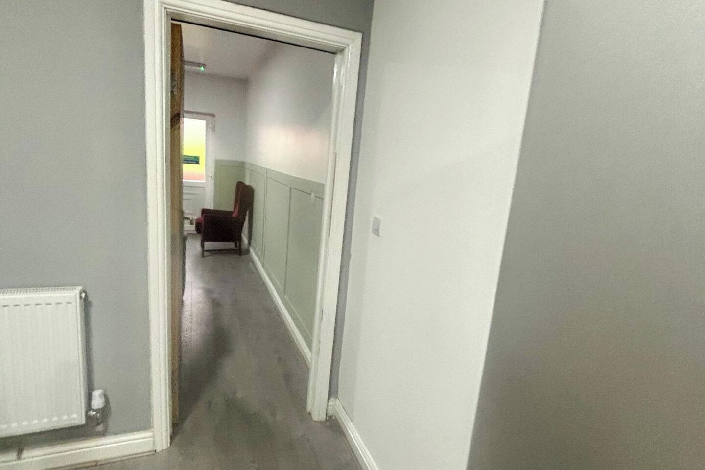 A hallway with a radiator, a chair, and a door leading to another room.