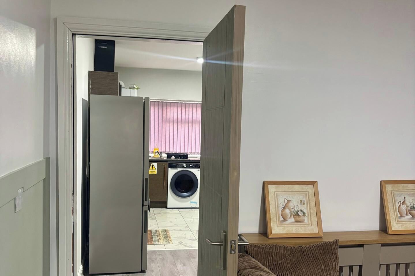Ein Zimmer mit einer Tür zu einer Küchenzeile, einer Waschmaschine und einem Tisch mit zwei gerahmten Bildern.