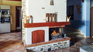Ein Kamin aus Stein mit hölzernem Sims, ein Fliesenboden und ein Küchenbereich mit Geräten.