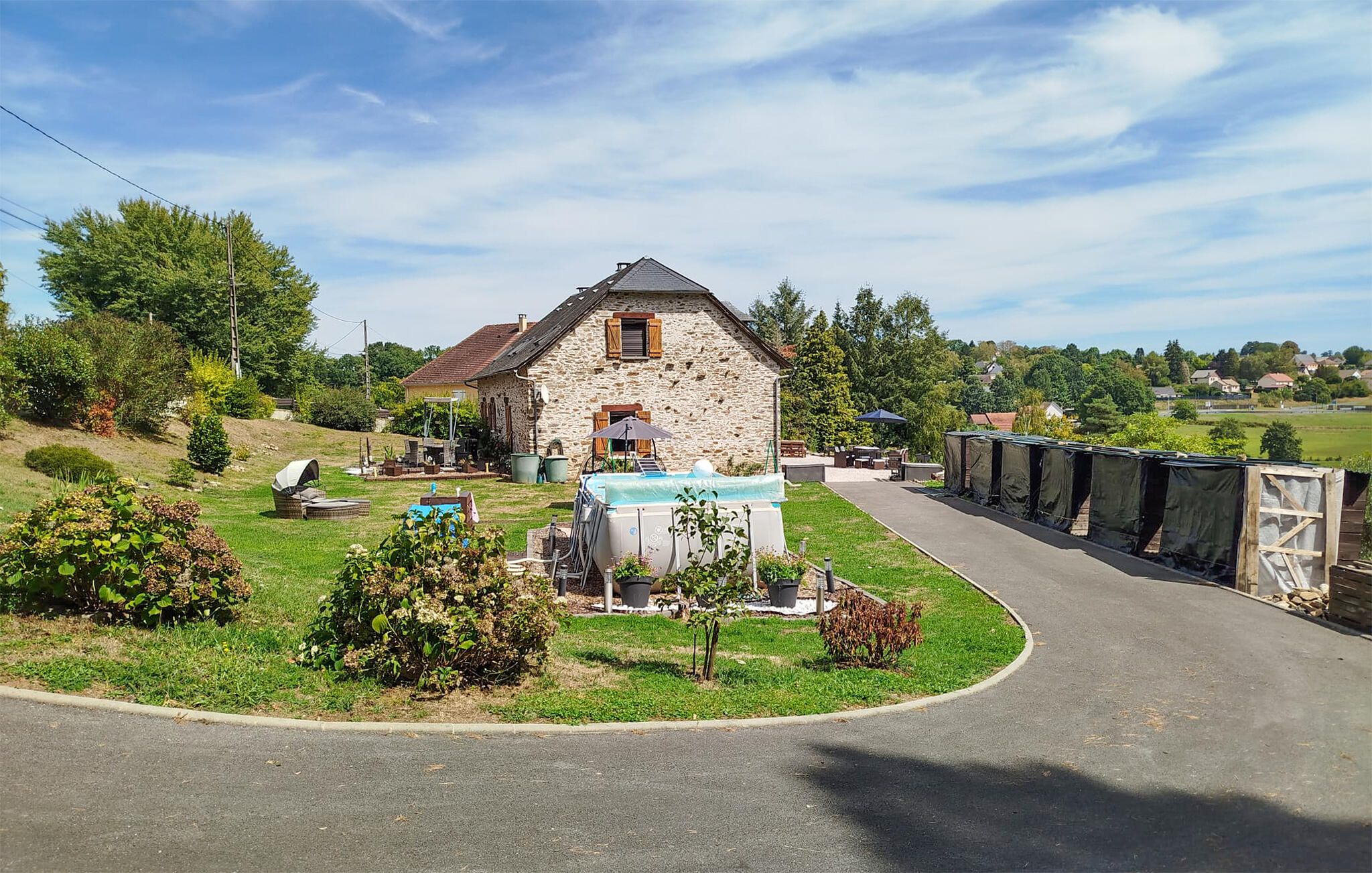 A stone house with a swimming pool, surrounded by a well-maintained lawn and a curved driveway.