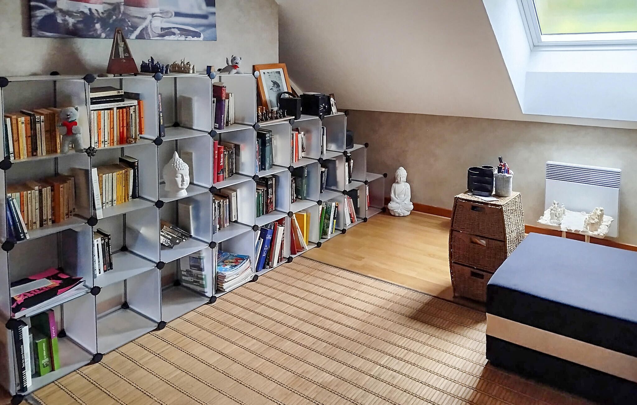 A room with a sloped ceiling, a bookshelf filled with books, a small Buddha statue, and a radiator.