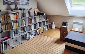 Ein Zimmer mit schrägem Dach, einem Bücherregal voller Bücher, einer kleinen Buddha-Statue und einer Heizung.