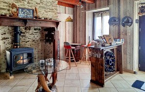 A rustic interior with a wood-burning stove, a round glass table, and a bar area with stools. - Maison avec piscine et jaccuzz (Saint-Jal)