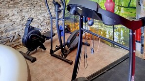 Ein Heimfitnessraum mit Trainingsgeräten, darunter ein Ergometer, ein Crosstrainer und Gewichte.
