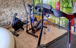 Ein Heimfitnessraum mit Trainingsgeräten, darunter ein Ergometer, ein Crosstrainer und Gewichte.