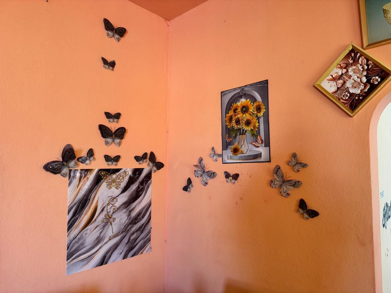 A wall with butterfly decorations, a framed picture of sunflowers, and a marble artwork.