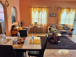 A living room with a sofa, a dining table with chairs, a fan, and a small table with a plant. - Mammee Bay Hideaway (St. Ann Parish)
