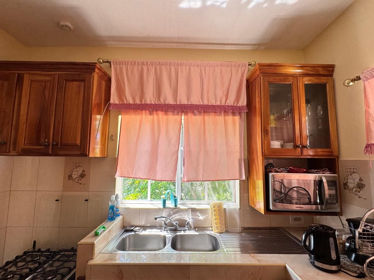 A kitchen with wooden cabinets, a double sink, a microwave, and a gas stove.