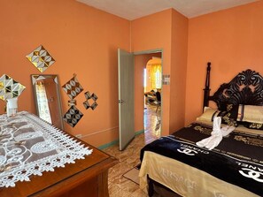 A hotel room with a bed, a wooden nightstand, a mirror, and a door leading to another room. - Mammee Bay Hideaway (St. Ann Parish)