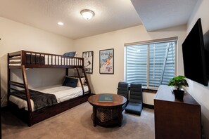 Ein Zimmer mit einem Etagenbett, einem Schreibtisch mit Pflanze, einem Stuhl und einem Fenster mit Jalousien.