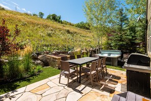 A patio with a stone table and chairs, a hot tub, and a grill area. - Private Backyard & Hot Tub | Minutes to Deer Valley, Jordanelle & Park City (Kamas)