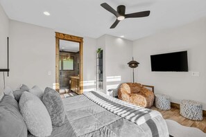 A modern bedroom with a bed, a ceiling fan, a TV, and a bathroom visible through an open door. - Vintage Vale at Eagles Nest - Views, yard games, hot tub, outdoor fireplace (Elk Park)