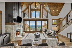 A spacious living room with a stone fireplace, comfortable seating, a television, and a view of the outdoors. - Vintage Vale at Eagles Nest - Views, yard games, hot tub, outdoor fireplace (Elk Park)