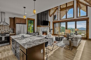 A spacious kitchen with a large island, a fireplace, and a dining area with a view. - Vintage Vale at Eagles Nest - Views, yard games, hot tub, outdoor fireplace (Elk Park)