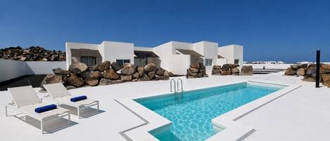 A modern outdoor pool area with lounge chairs and a clear blue sky.