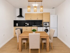 A modern kitchen with wooden cabinets, a black range hood, a microwave, a washing machine, and a dining table with chairs. - Standard Suite · 2 bedrooms Adults Only (Costa Teguise)