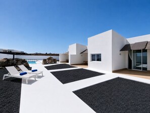 Zona exterior moderna amb seients lounge blancs, una piscina i un cel serè.