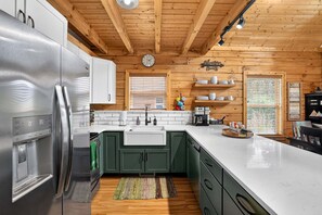 Une cuisine moderne avec un réfrigérateur en acier inoxydable, des armoires vertes, un plan de travail blanc et des poutres en bois au plafond.