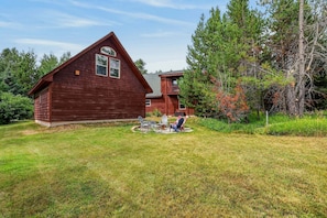 A wooden cabin with a two-story structure, a deck with outdoor seating, and a well-maintained lawn. - White Fir Cabin | Hot Tub | Fire Pit | Near Tamarack (Donnelly)