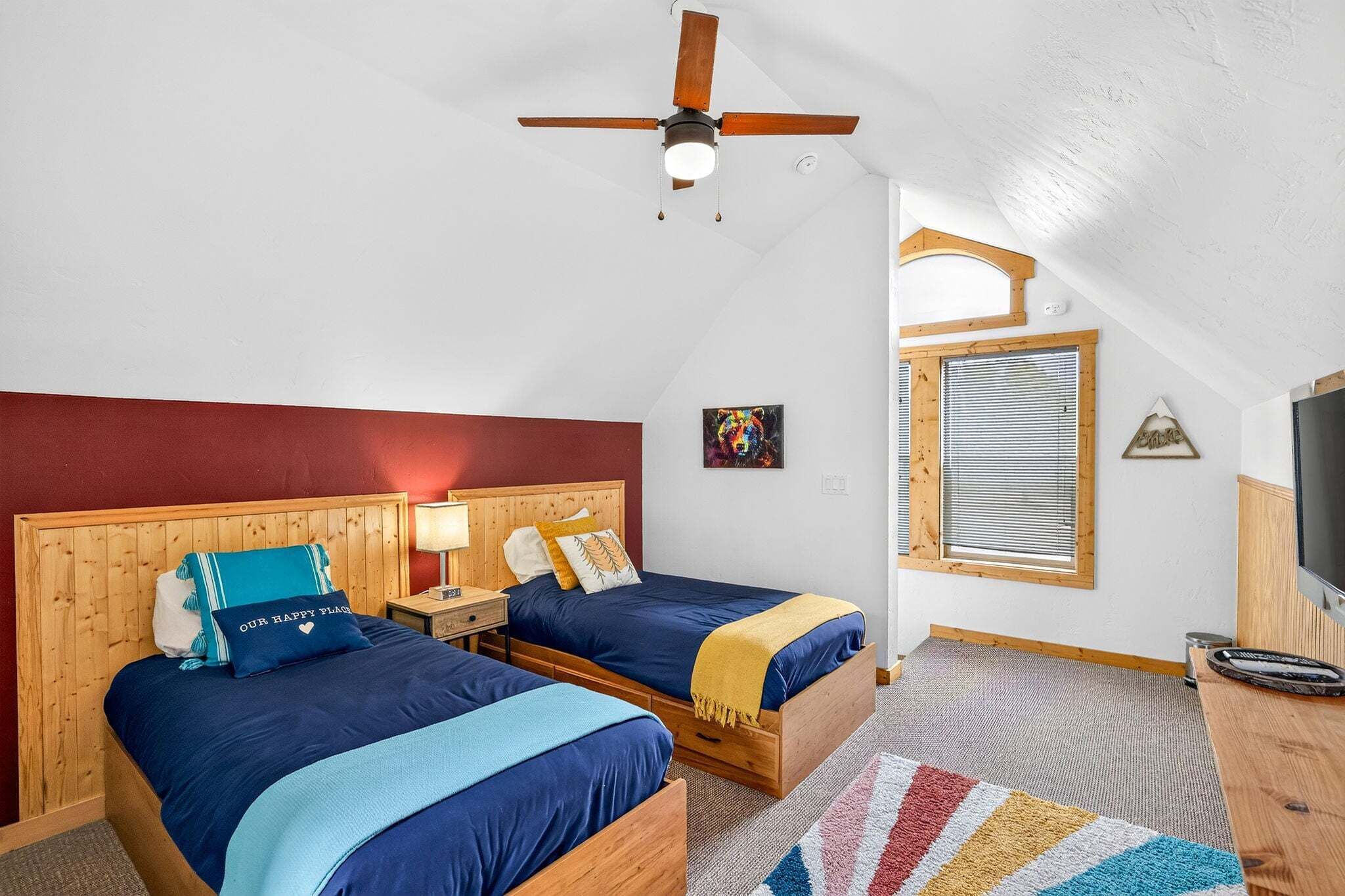 A bedroom with two beds, a ceiling fan, a window with blinds, and a television on a wooden stand.