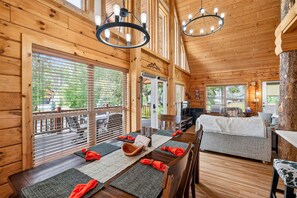 A wooden cabin interior with a dining area, a living room, and a view of the outdoors. - White Fir Cabin | Hot Tub | Fire Pit | Near Tamarack (Donnelly)