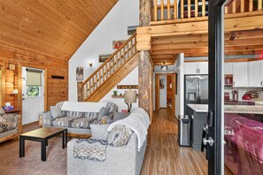 A cozy living room with a staircase, wooden walls, and a kitchen area. - White Fir Cabin | Hot Tub | Fire Pit | Near Tamarack (Donnelly)