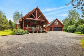 A large log cabin with a covered porch, a garage, and a gravel driveway. - White Fir Cabin | Hot Tub | Fire Pit | Near Tamarack (Donnelly)