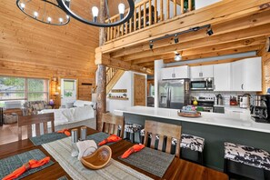 A modern cabin interior with a dining area, kitchen, and a loft bedroom. - White Fir Cabin | Hot Tub | Fire Pit | Near Tamarack (Donnelly)