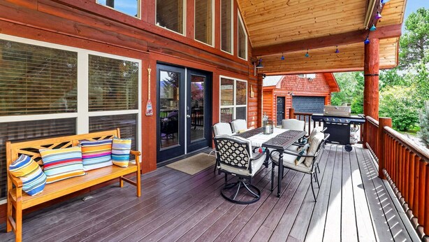 En træterrasse med bænk og udendørs møbler, grill og udsigt til et hus i baggrunden.