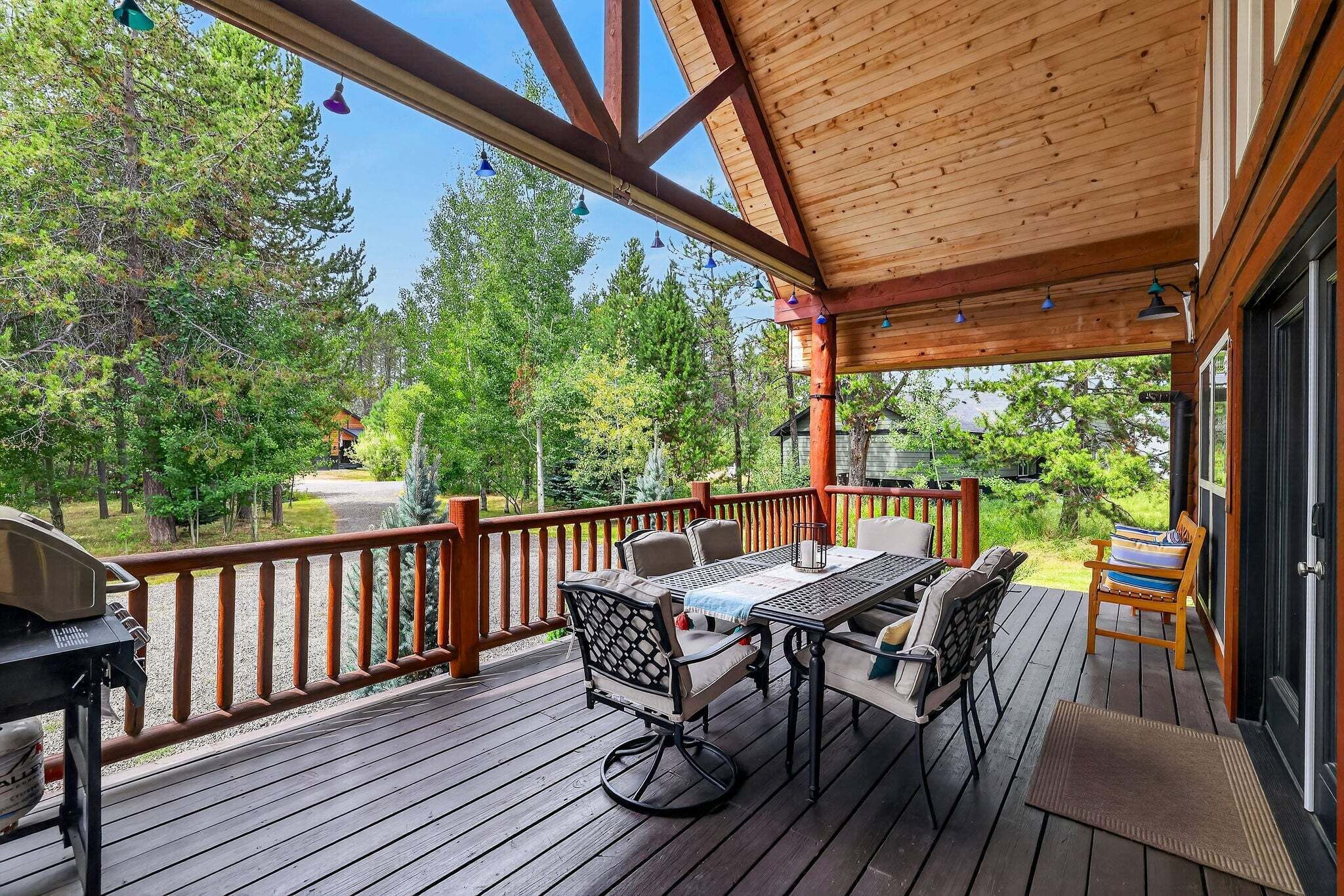 Eine Holzdielen-Terrasse mit Tisch und Stühlen, umgeben von einem Geländer, mit Blick auf einen bewaldeten Bereich.