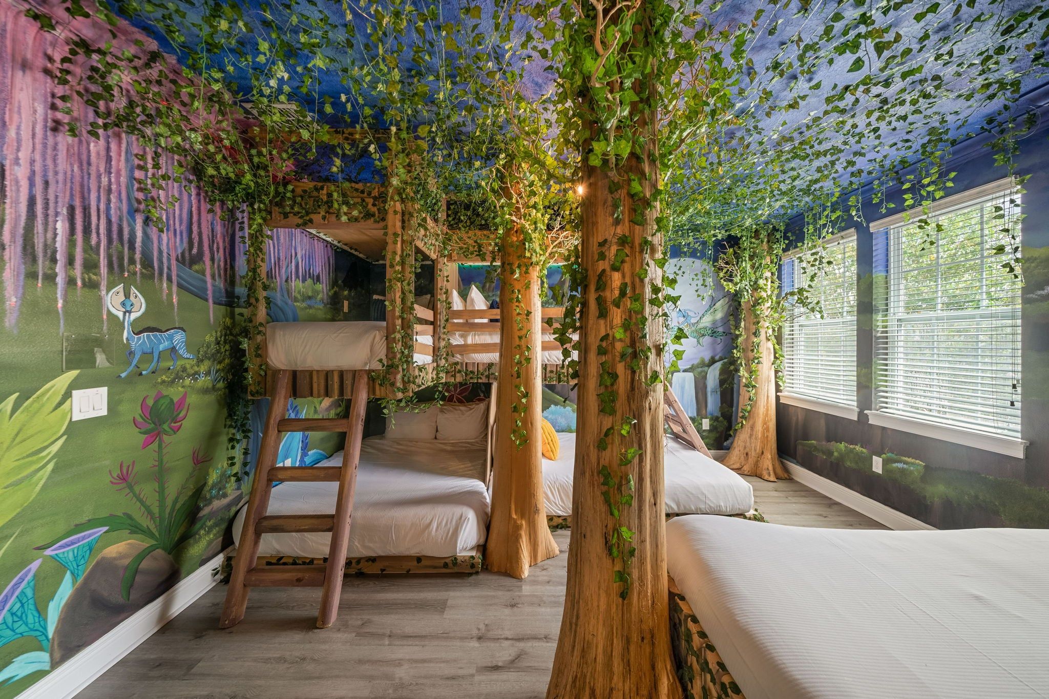 Un dormitorio tipo casa del árbol con literas, una escalera y un mural con un dinosaurio.