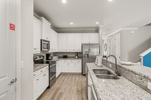 A modern kitchen with white cabinets, stainless steel appliances, granite countertops, and a double sink. - Legends Coastal Cottage, Arcade, Golf simulator, Near Disney (Kissimmee)