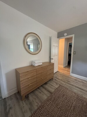 A room with a wooden dresser, a round mirror, and a door leading to another room.