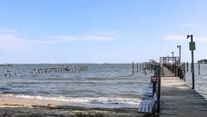 Eine Holzstege, der sich über ruhiges Wasser zu einem Sandstrand erstreckt.