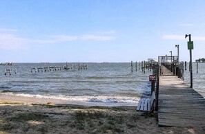 Eine Holzstege, der sich über ruhiges Wasser zu einem Sandstrand erstreckt.