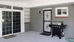 Ein überdachter Patio-Bereich mit einer Schiebetür, einer schwarzen Grillstation und einem kleinen Fenster.