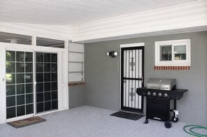 Ein überdachter Patio-Bereich mit einer Schiebetür, einer schwarzen Grillstation und einem kleinen Fenster.