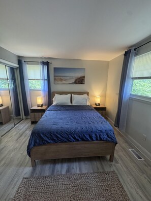 Ein Schlafzimmer mit einem großen Bett, zwei Nachttischen mit Lampen, einem Bild an der Wand und Blick ins Freie durch das Fenster.