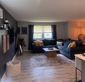 A modern living room with a dark blue sofa, a wooden coffee table, and a large window with curtains. - Welcome to Getaway on the Bay | Your Waterfront Annapolis Escape (Annapolis)