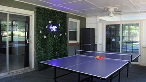 Ein Tischtennistisch in einem Raum mit grüner Wand, einer Neonreklame und einem Deckenventilator.