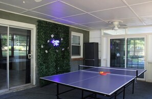 Ein Tischtennistisch in einem Raum mit grüner Wand, einer Neonreklame und einem Deckenventilator.