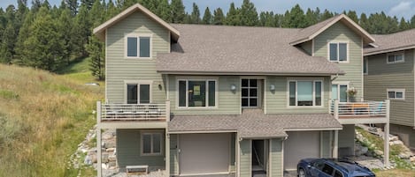 Une maison à deux étages avec un garage, une véranda et une allée où est garée une voiture.