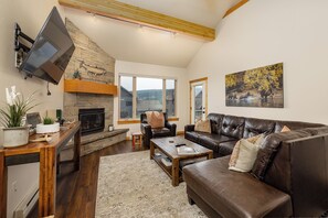A living room with a stone fireplace, leather sofa, and a television mounted on the wall. - New Listing! | Private Hot Tub & Minutes to Big Sky Resort and Town Center (Big Sky)