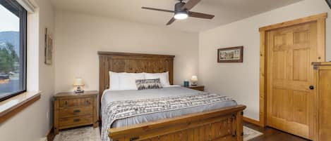 Un dormitorio con una cama de madera, un ventilador de techo, una ventana y una puerta.