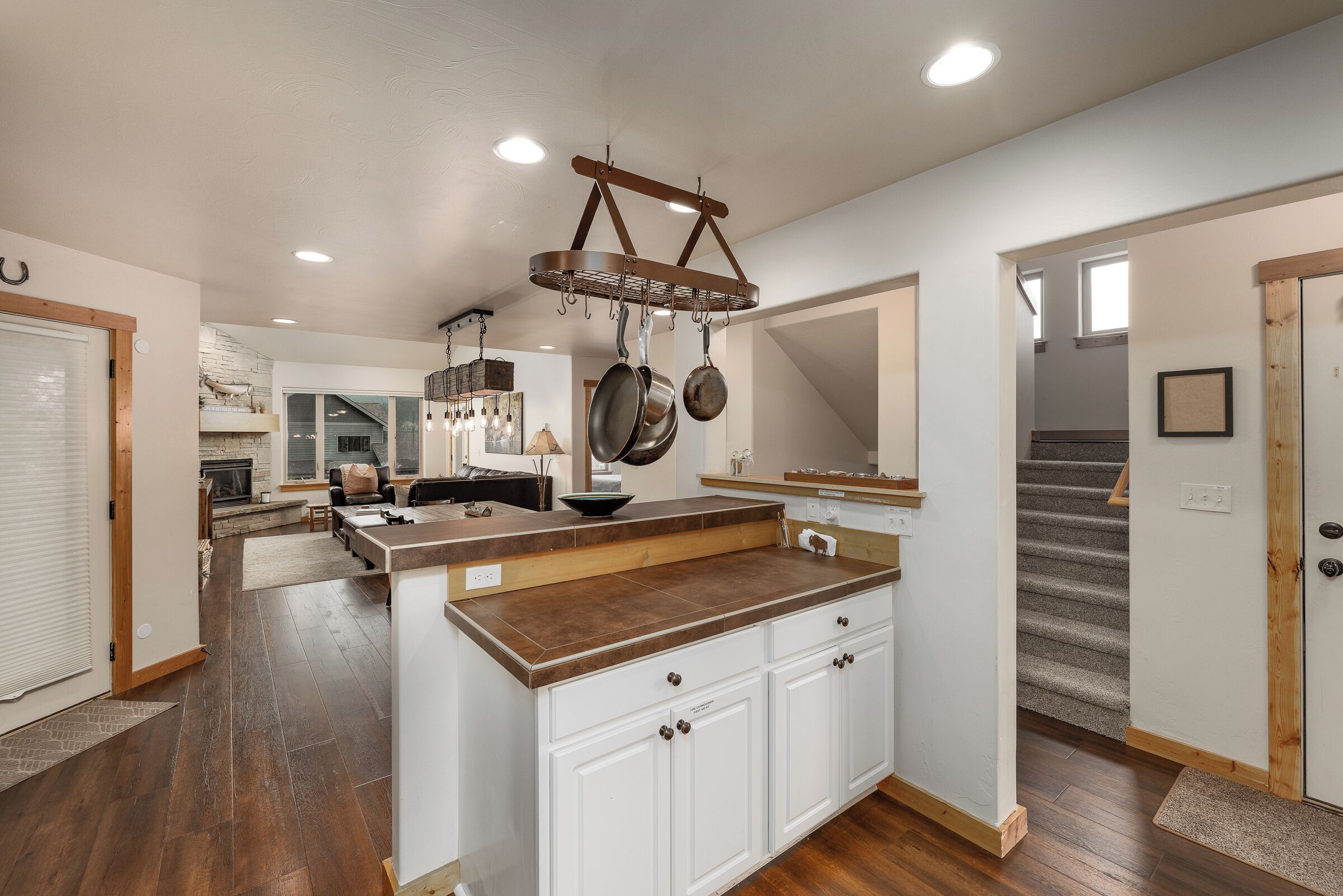 A kitchen with a central island, wooden flooring, and a hanging pot rack.